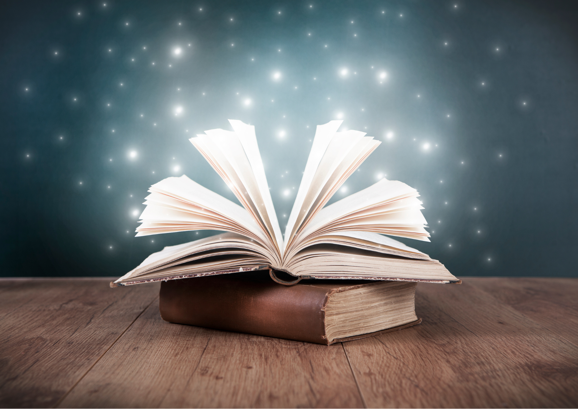 2 dicke Bücher in braunem Ledereinband liegen übereinander auf einer Tischplatte aus Holz. Das Buch das oben liegt, ist geöffnet und die Seiten fallen locker auseinander. Helle Lichtpunkte schimmern über den offenen Buchseiten.